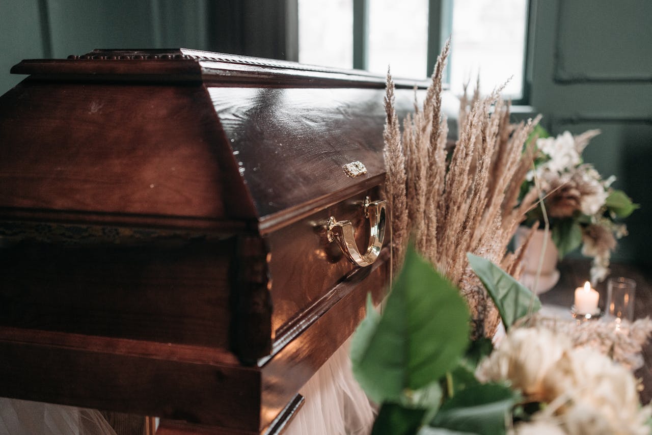 A beautiful funeral display featuring a wooden coffin with flowers and candles indoors.